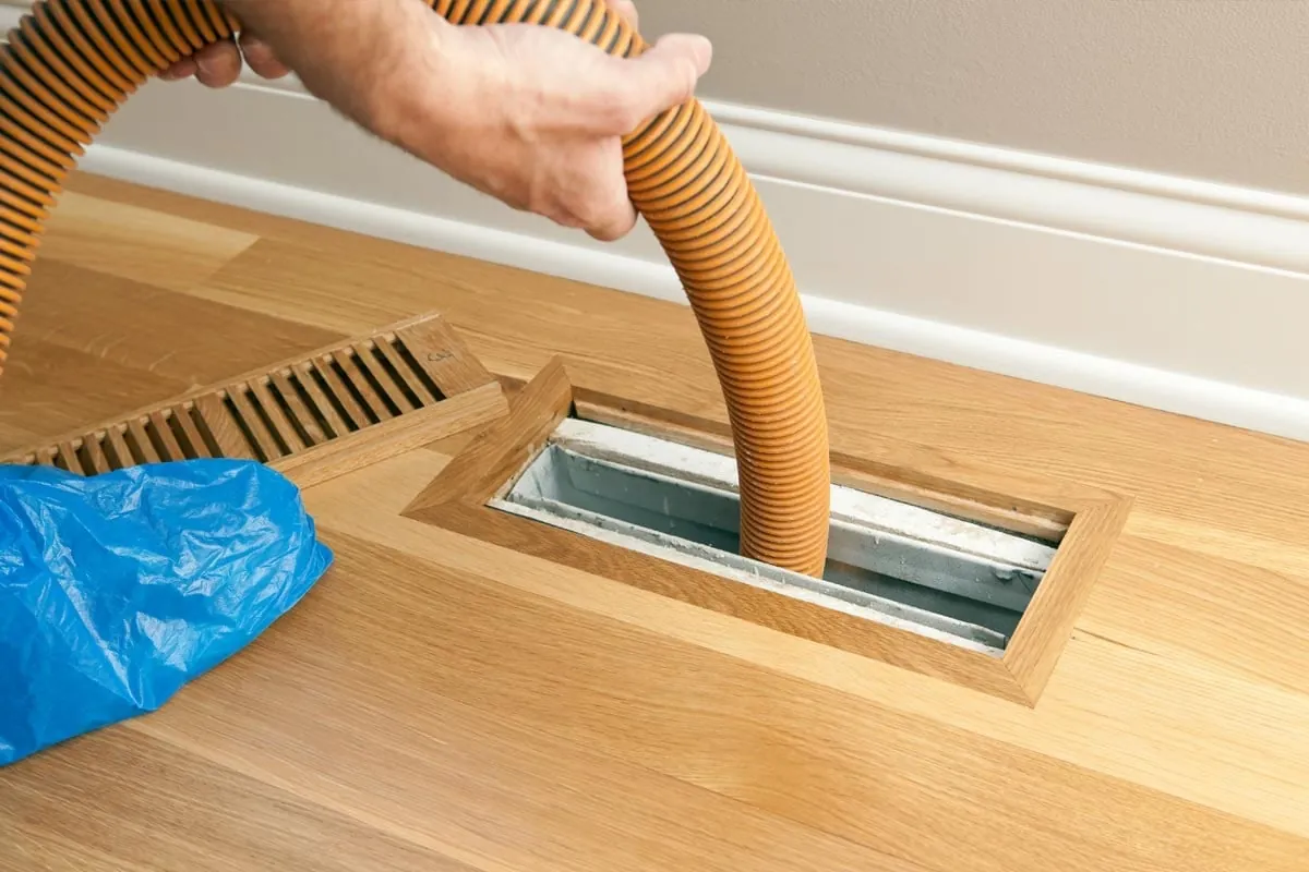 Technician vacuuming a floor vent during HVAC service